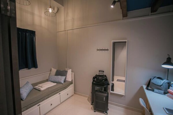 Habitación de hotel pequeña con una cama, un escritorio, una silla, una maleta y un espejo.