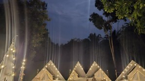 Une rangée de tentes illuminées de guirlandes lumineuses, se dressant sur fond d’arbres et d’une cascade.