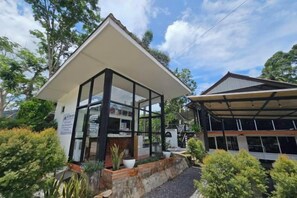 A modern building with a glass enclosure and a covered area, surrounded by greenery.