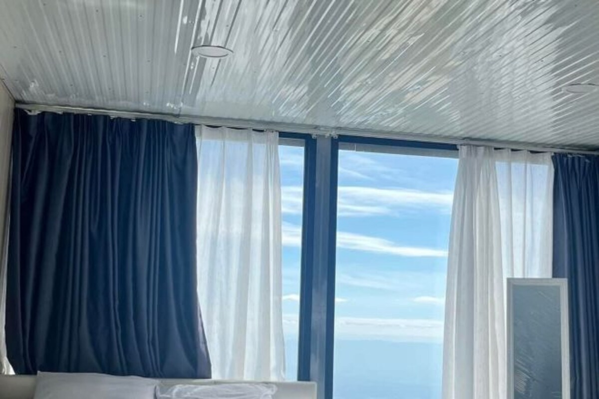 A room with a large window, white curtains, and a view of the sky.