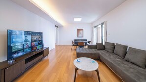 A modern living room with a flat-screen TV, a sofa, a coffee table, and a dining area with chairs and a table. - Tyms Family 3BR 2BA Apt Xujiahui Metro (Shanghai)