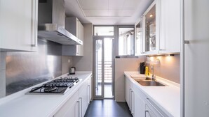 A modern kitchen with white cabinets, a stainless steel range hood, a gas stove, a sink, and a window overlooking a balcony. - Tyms Family 3BR 2BA Apt Xujiahui Metro (Shanghai)