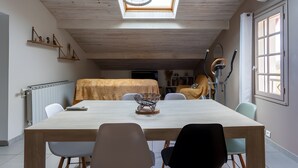 Un espace repas comprenant une table, des chaises, un ventilateur de plafond, un radiateur et une lucarne.