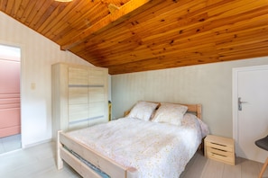 Un dormitorio con techo de madera, una cama con ropa de cama estampada, un armario y una mesita de noche pequeña.