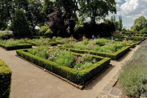 A formal garden with geometrically shaped flower beds and a paved walkway. - StarNest Shepherd's Bush (London)