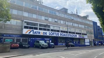 Un edificio con un cartel que indica 'Natrae Loftus Road Stadium' y varios coches estacionados.