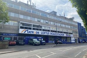 A building with a sign for 'Natrae Loftus Road Stadium' and several parked cars. - StarNest Shepherd's Bush (London)