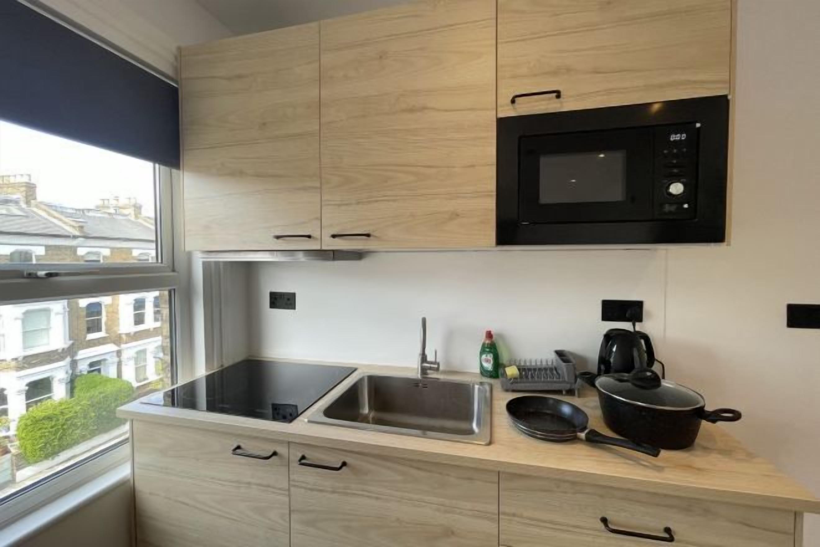 A modern kitchen with wooden cabinets, a black microwave, a sink, and a window with a view of buildings.