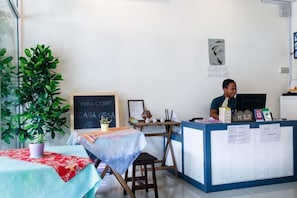 A reception desk with a chalkboard sign, a potted plant, and a table with a red tablecloth. - Casa Casa Guesthouse Semporna (Semporna)