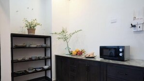 A kitchen with dark cabinets, a marble countertop, a microwave, and a shelf with dishes and a plant. - Signy House Sai Gon Center - Nguyen Binh Khiem (Ho Chi Minh City)