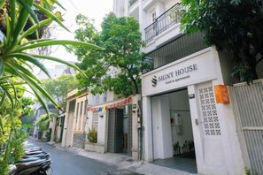 A hotel named 'Signy House' with a signboard, a gated entrance, and a street view with parked scooters.