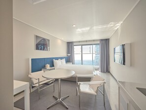 A modern hotel room with a large bed, a desk, and a chair. There is a window with a view of the sea and a cityscape. - YCollection HaeundaeBeach (Busan)