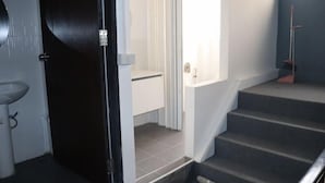 A staircase leading to a landing with a white wall and a door on the left. - The Moment hostel (Bangkok)