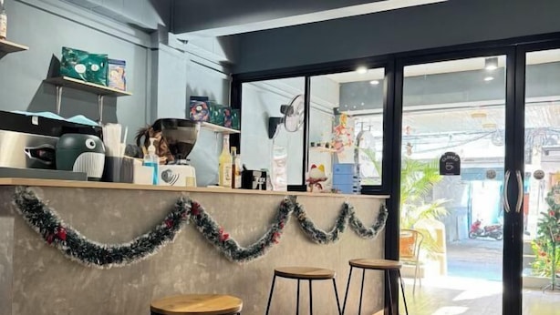 A modern bar area with a counter, stools, and a view of the street through large windows. - The Moment hostel (Bangkok)