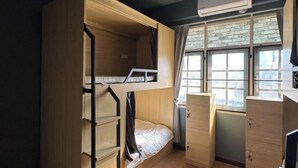 A bunk bed room with a desk and drawers, a window with curtains, and an air conditioning unit. - The Moment hostel (Bangkok)