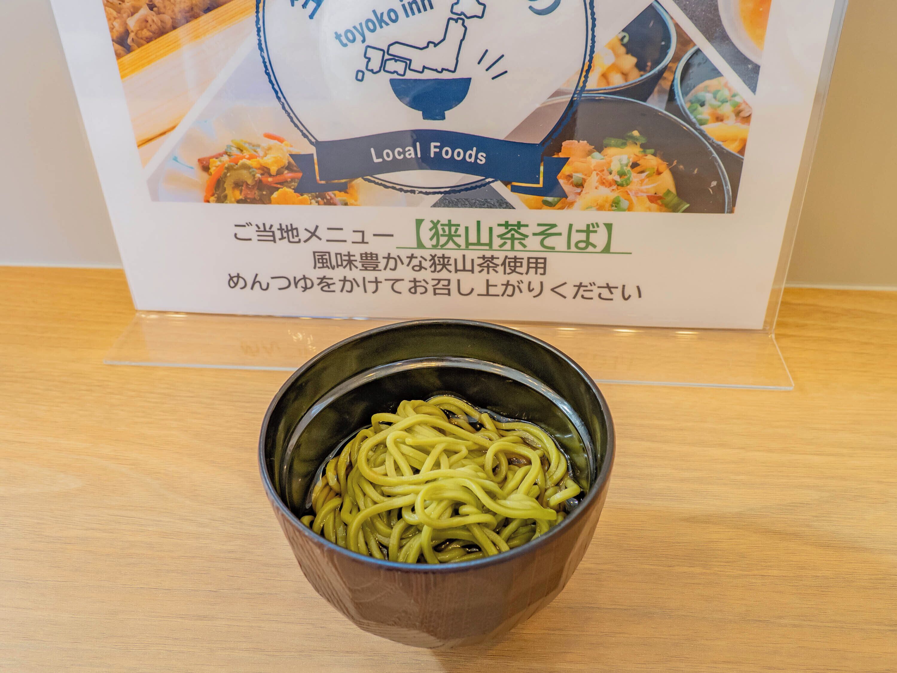 A bowl of noodles on a wooden table with a sign in the background.
