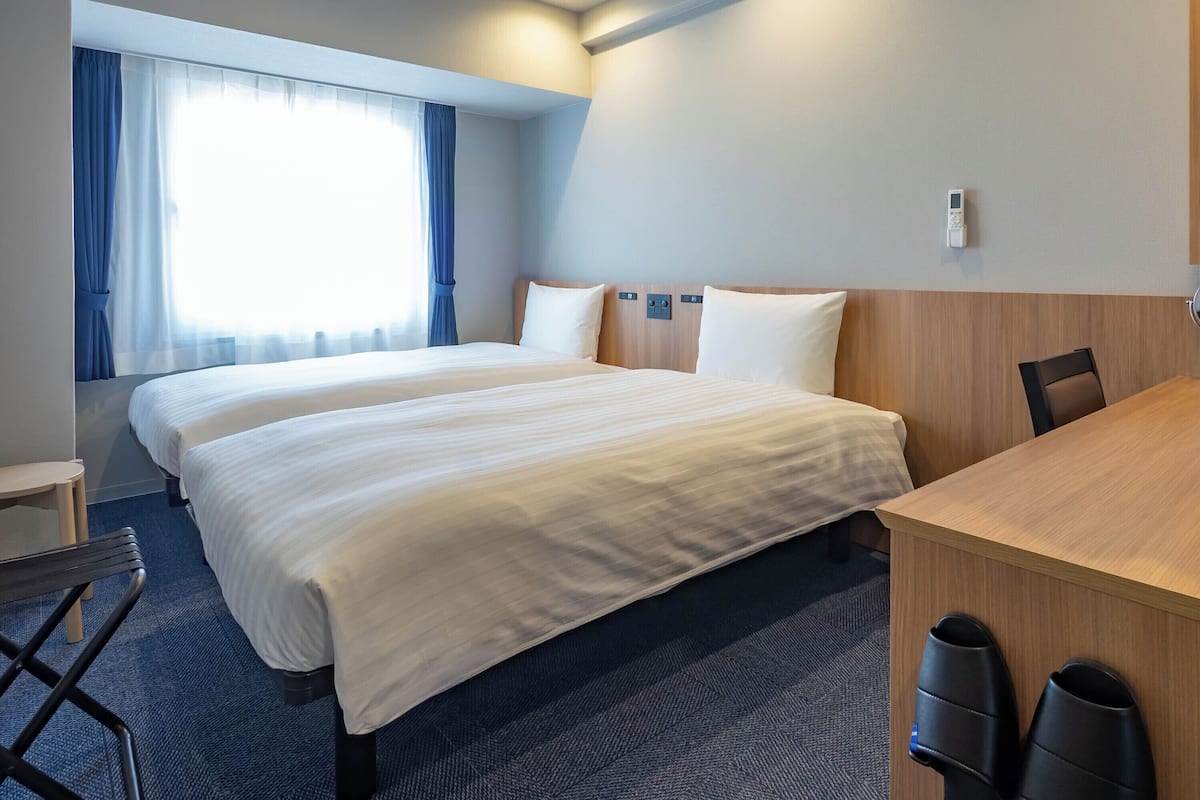 A hotel room with two beds, a desk, and a chair.