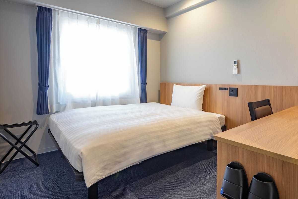A hotel room with a bed, a desk, a chair, and a window with curtains.