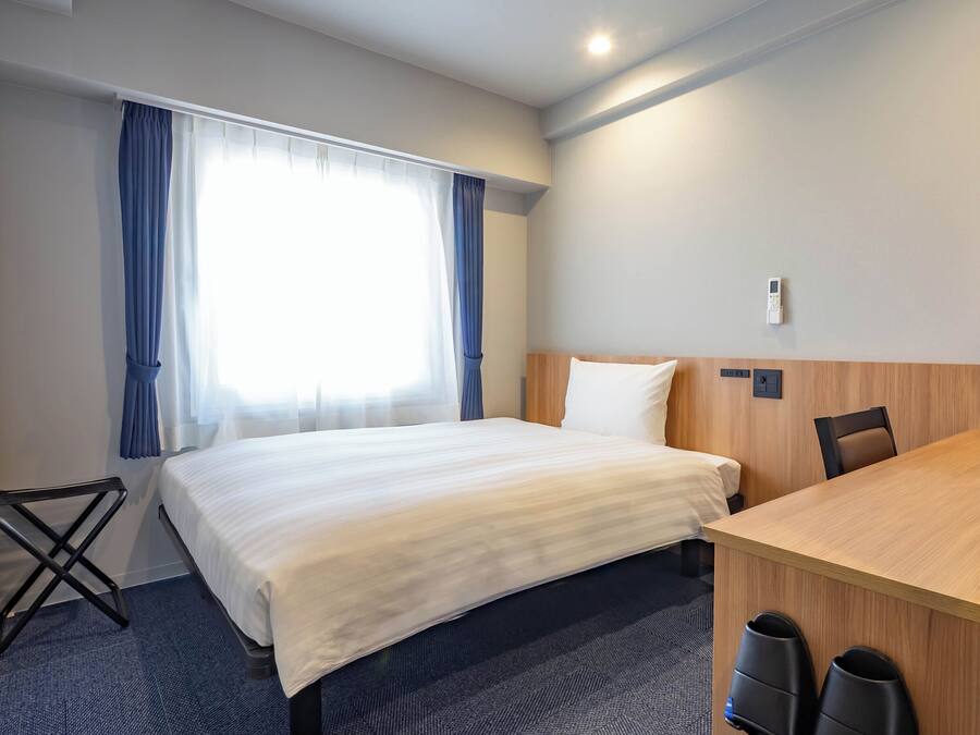 Habitación de hotel con cama, escritorio, silla y ventana con cortinas.