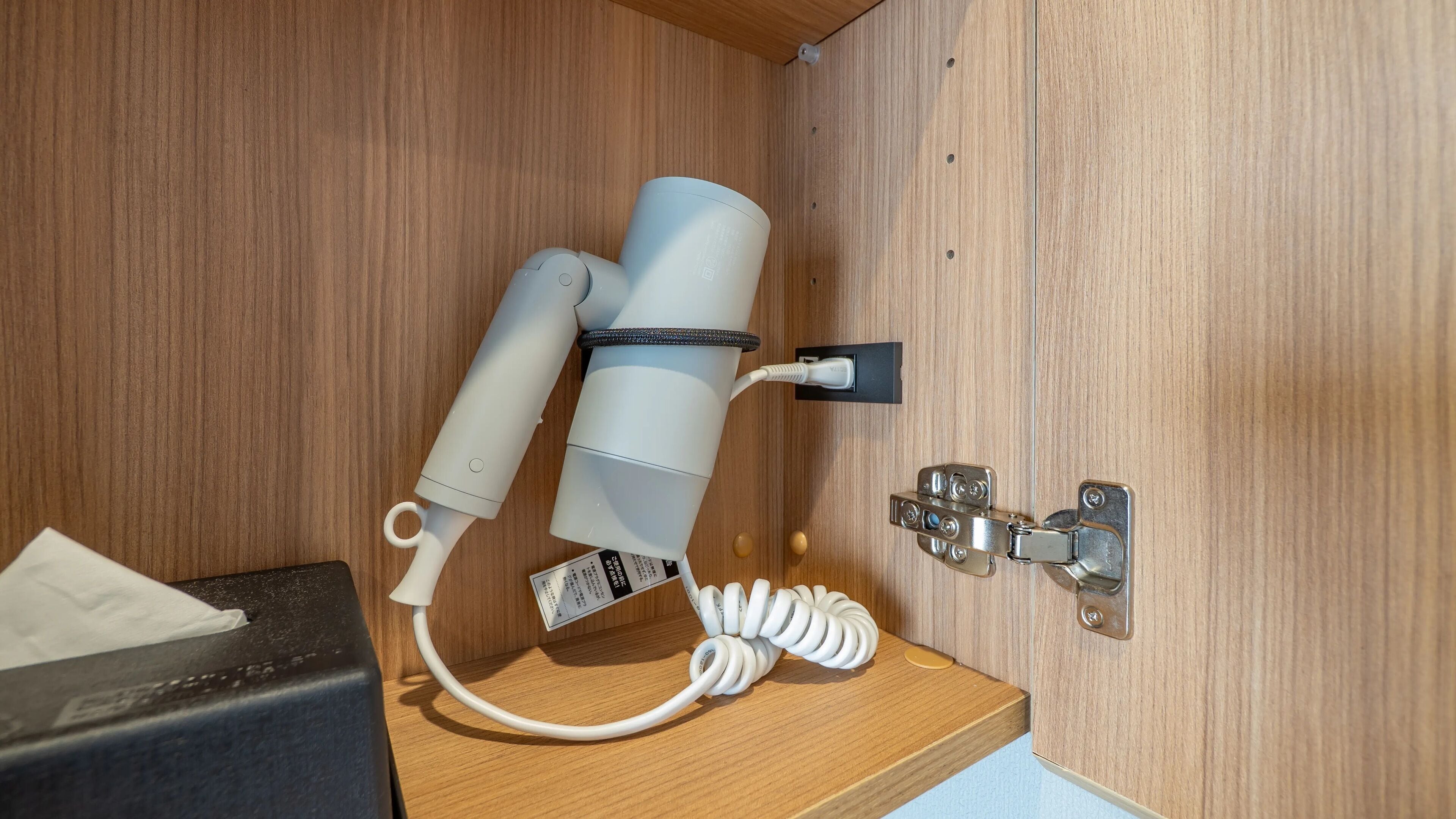 A hairdryer and a curling iron on a wooden shelf, connected to a power outlet.
