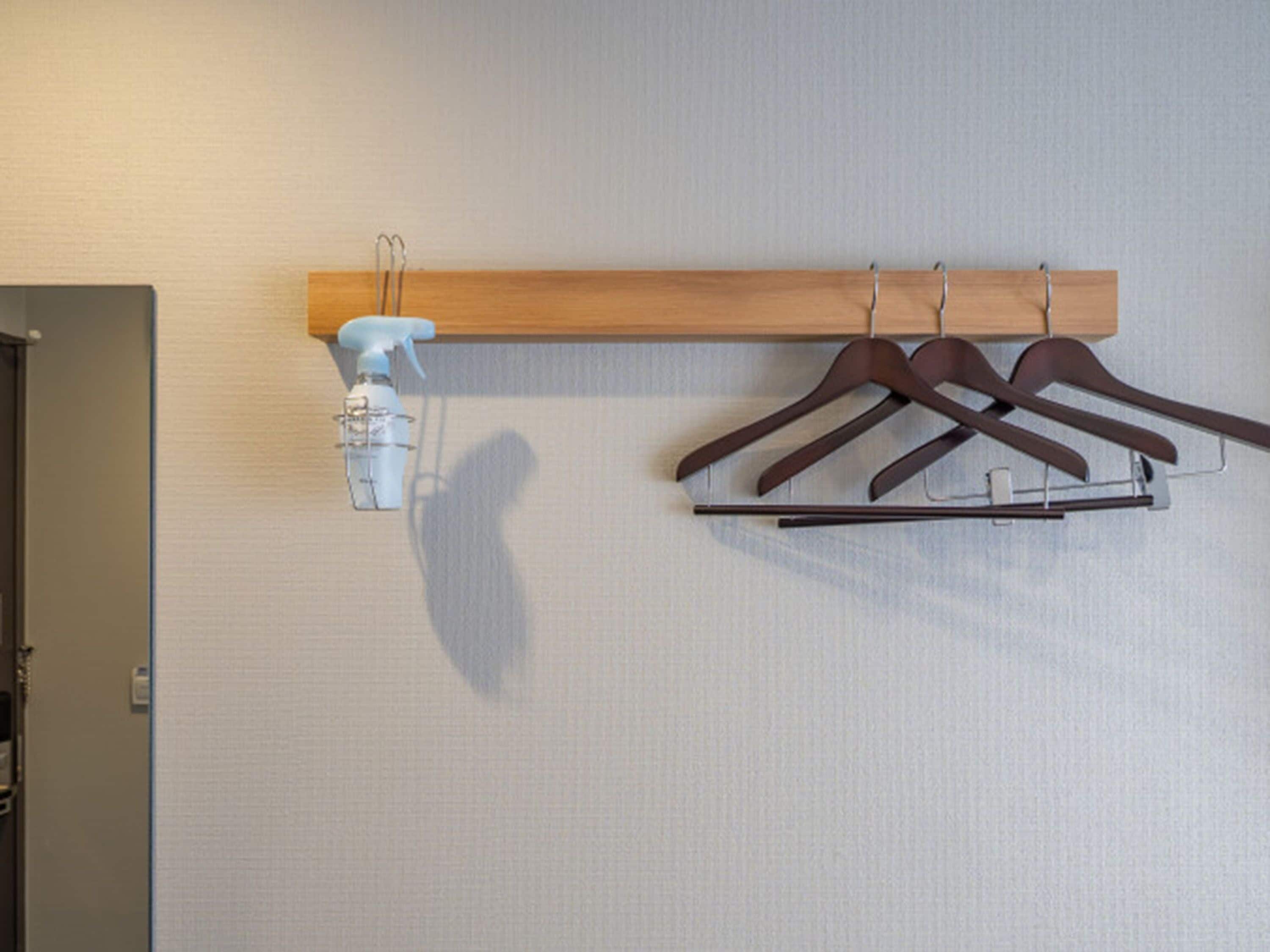 A wall-mounted wooden rack with three brown hangers and a white spray bottle.