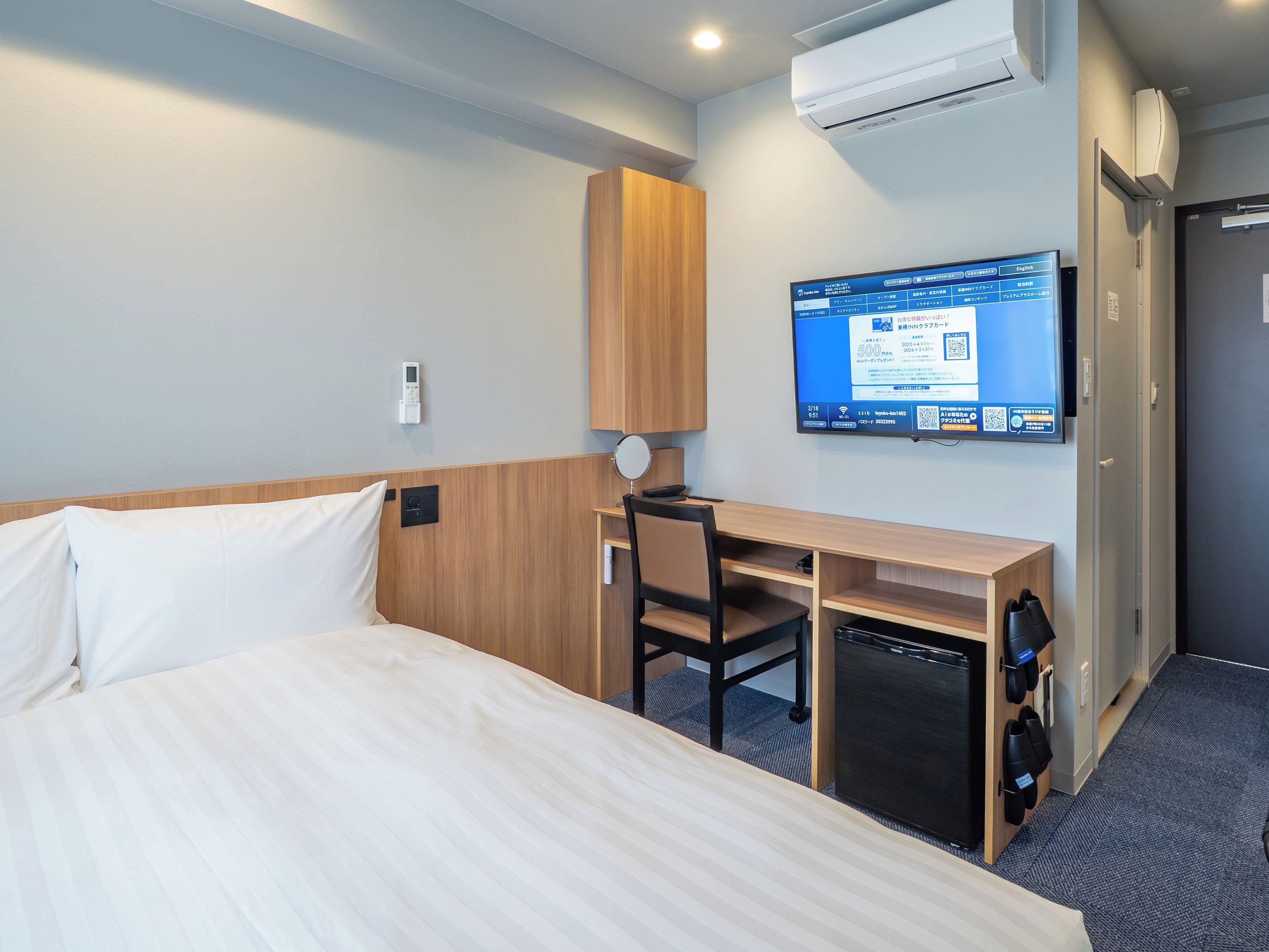 Ein Hotelzimmer mit einem Bett, einem Schreibtisch, einem Stuhl, einem Fernseher und einer Klimaanlage.