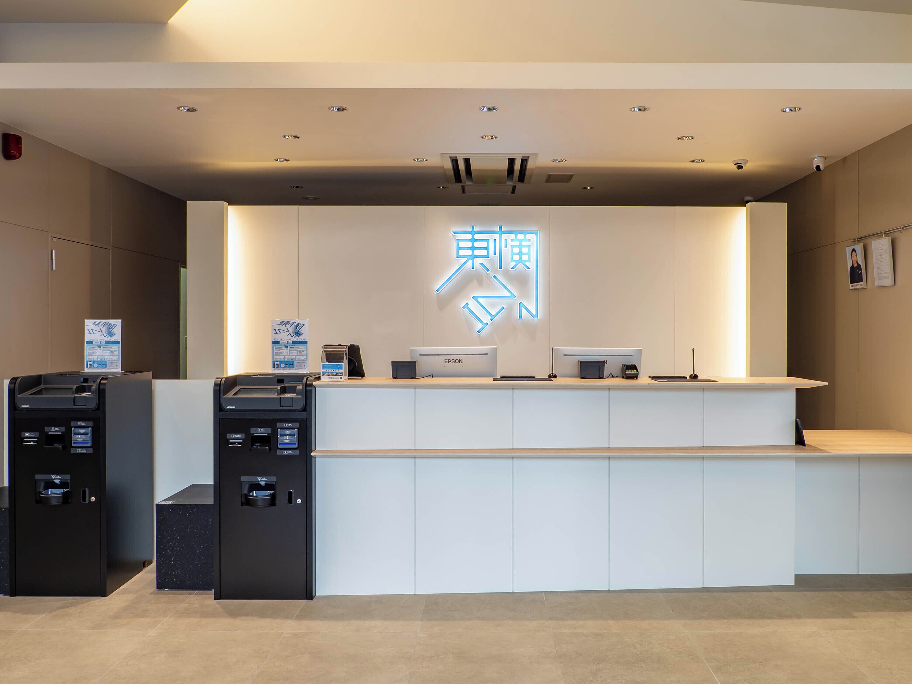 A reception desk with a neon sign, a printer, a cash machine, and a wall-mounted sign.