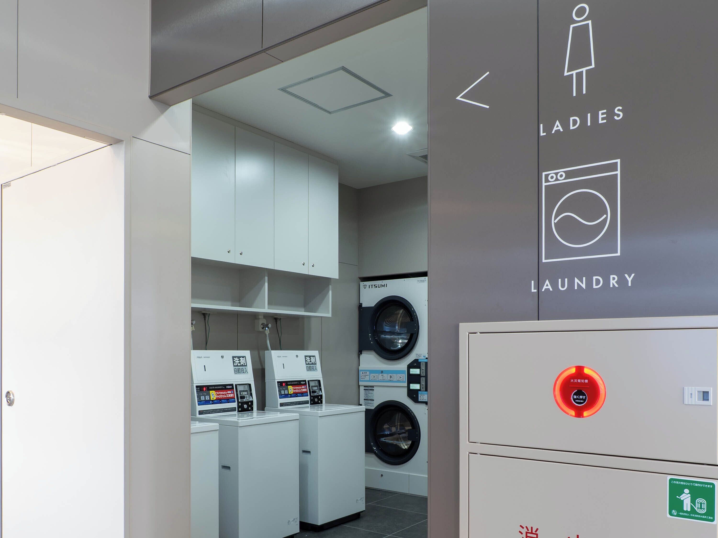 Un moderno cuarto de lavandería con varias lavadoras y secadoras, un panel de control y un letrero que indica servicios de lavandería para mujeres.