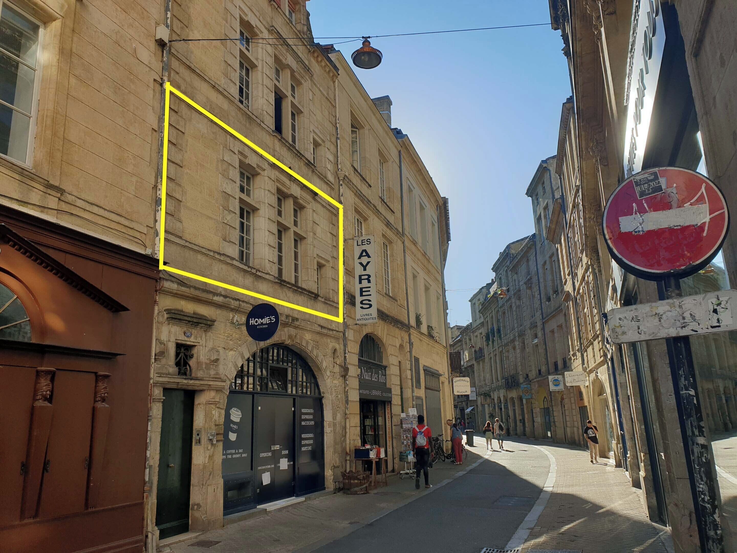 Une vue de rue avec un bâtiment sur lequel on peut lire les inscriptions « LES AYES » et « HOME'S » au rez-de-chaussée.