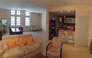 A spacious living room with a beige sofa, a dining table, and a kitchen area with bar stools.