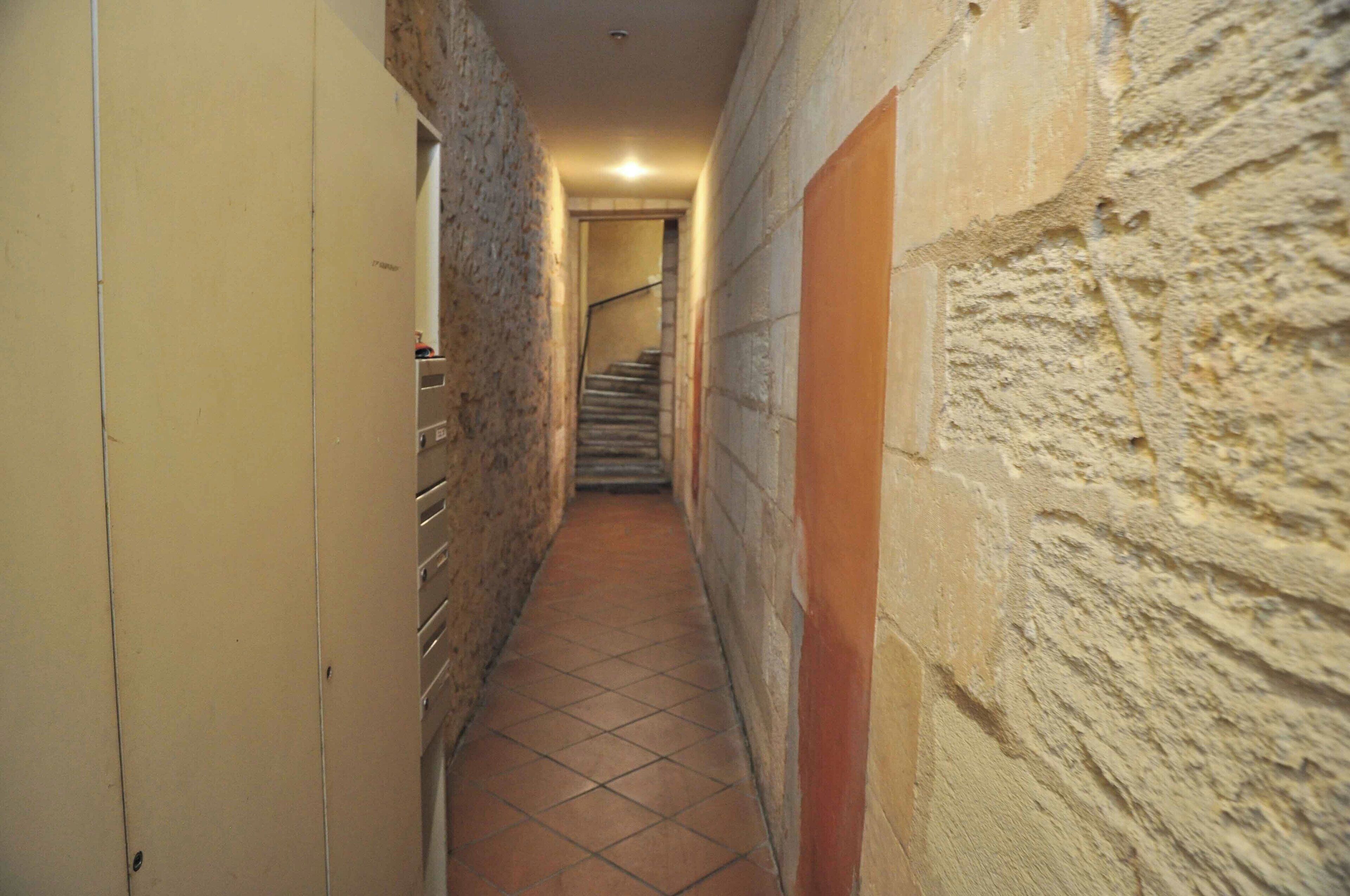Ein schmales Treppenhaus mit Fliesenboden, Steinwänden und einer Treppe am Ende.