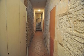 A narrow hallway with tiled flooring, stone walls, and a staircase at the end.