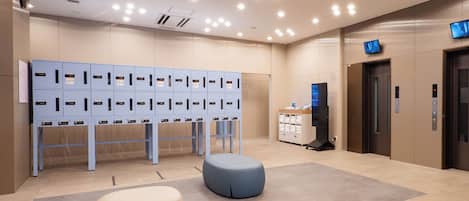 A modern lobby with a row of lockers, a reception desk, and an elevator.