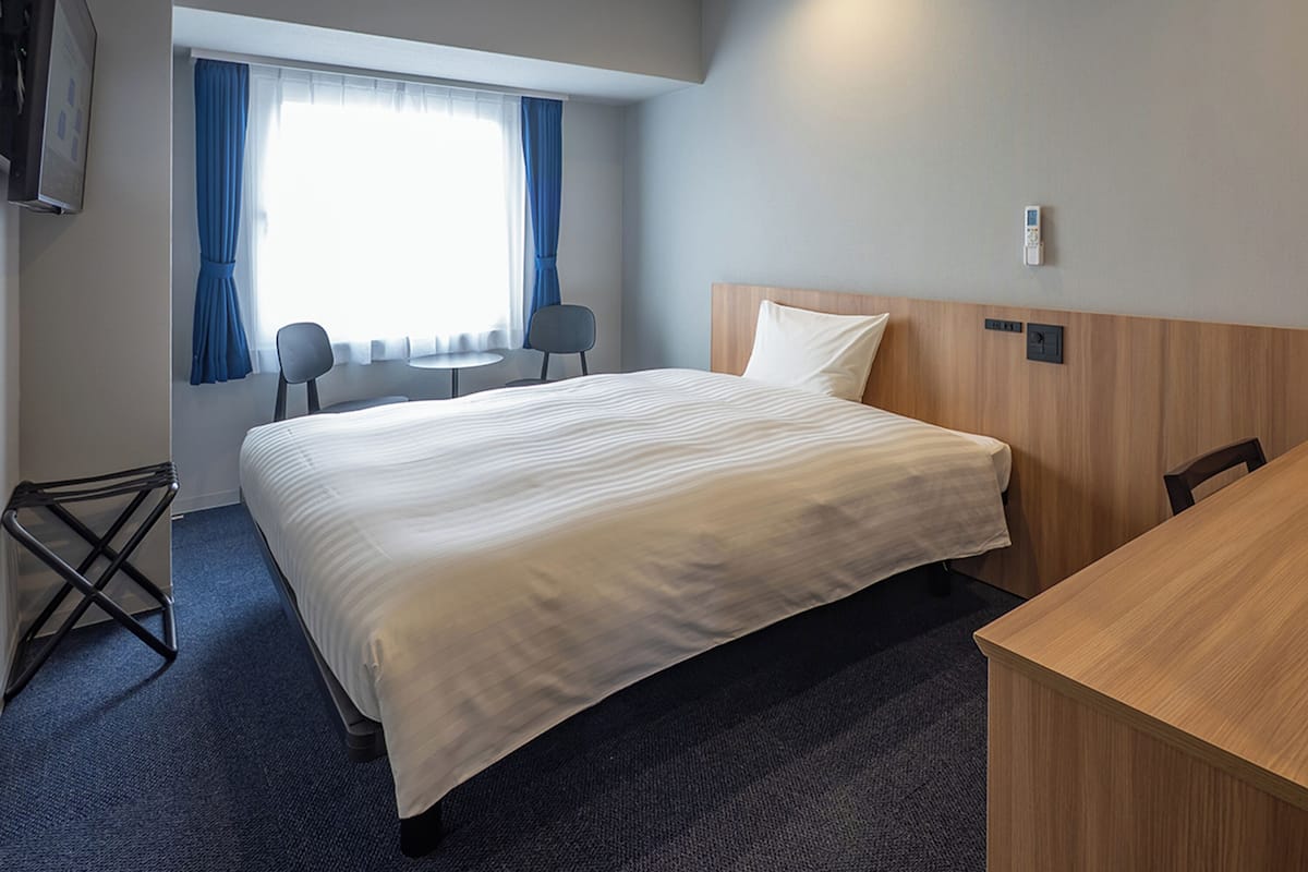Habitación de hotel con una cama grande, un escritorio, una silla, un televisor y una ventana con cortinas.