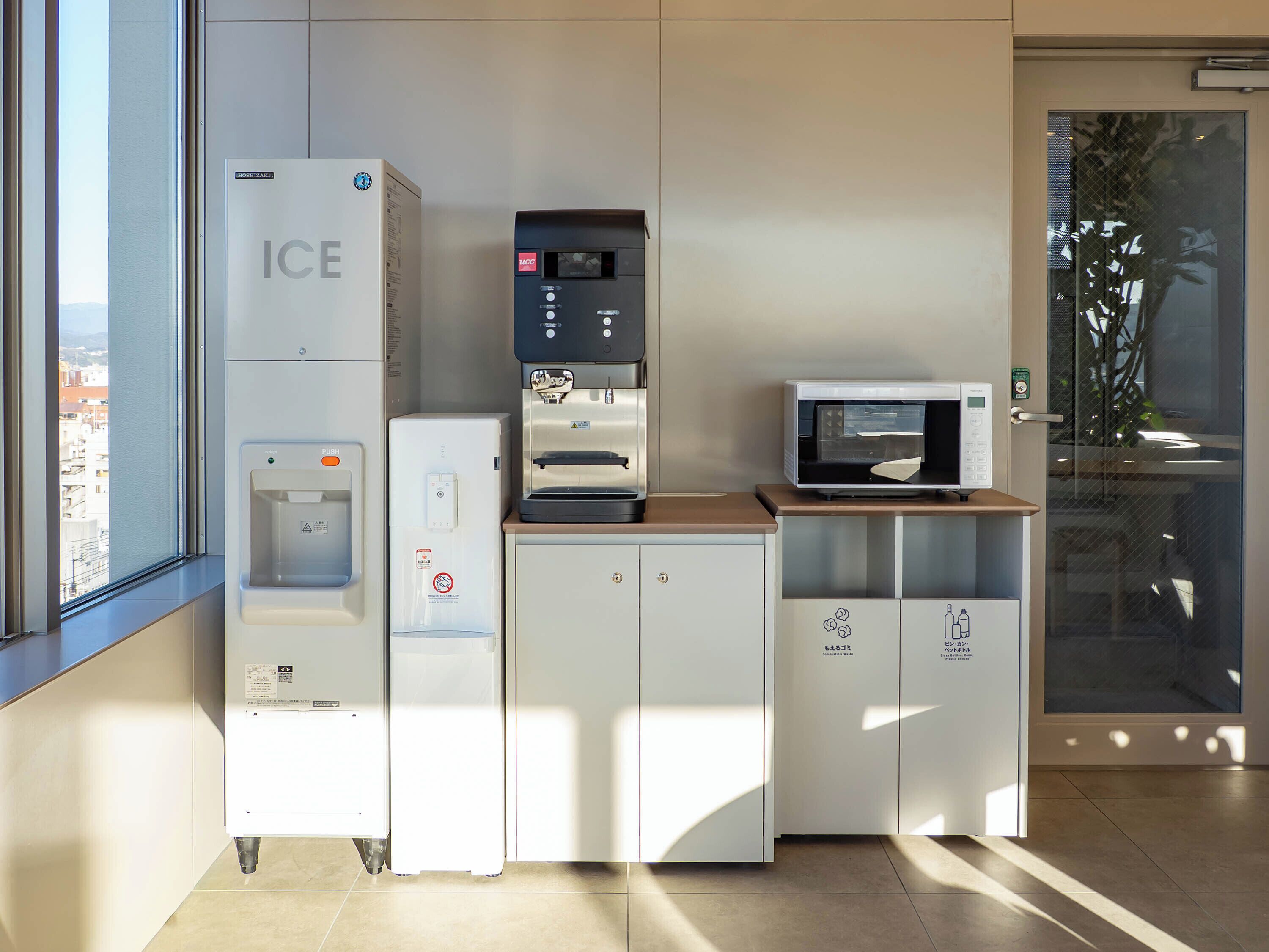 Eine Küchenzeile mit Eisspender, einer Kaffeemaschine, einer Mikrowelle und Schränken mit Recycling-Symbolen.