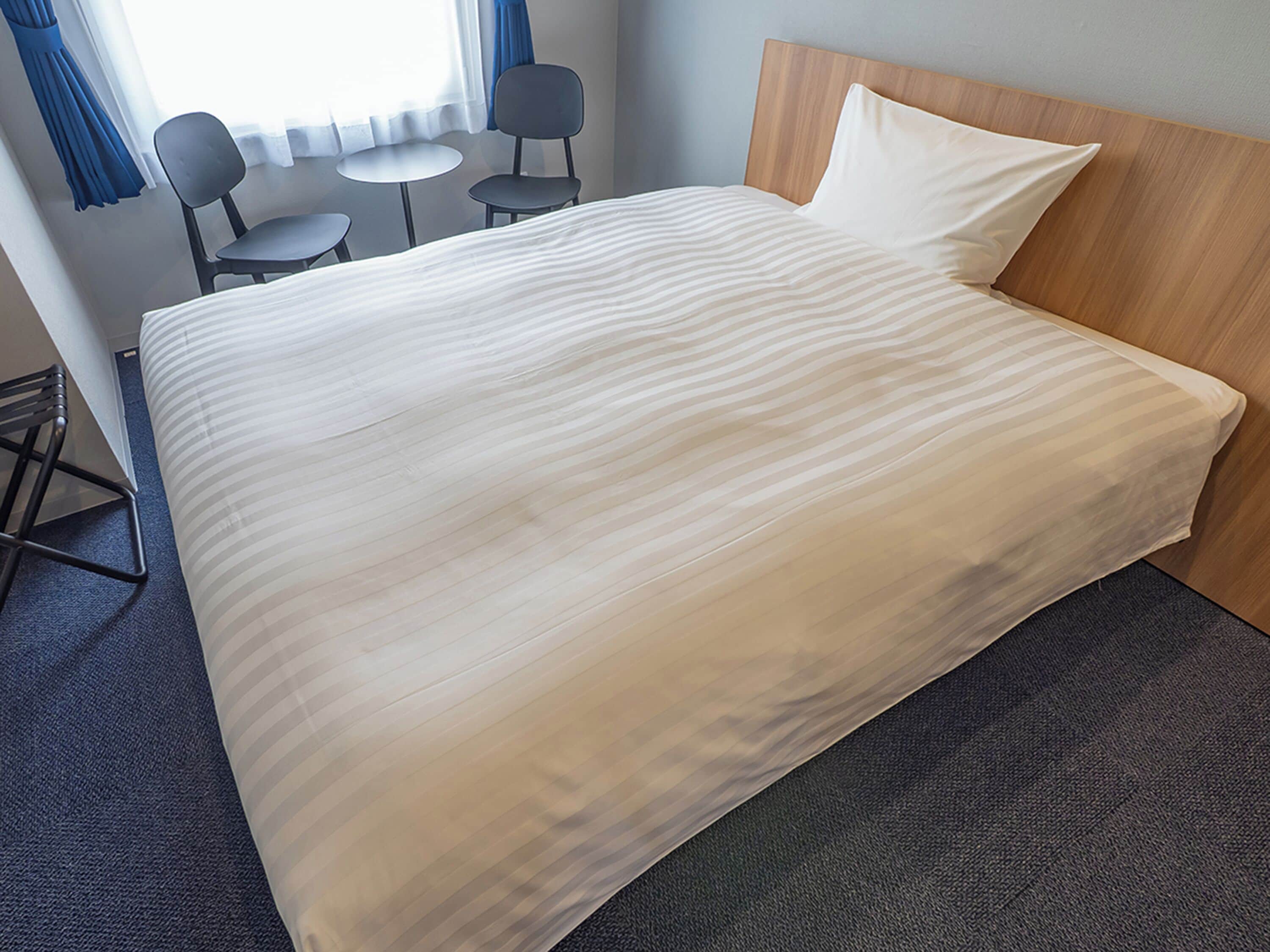 A hotel room with a large bed, a wooden headboard, a small round table, two chairs, and a window with curtains.