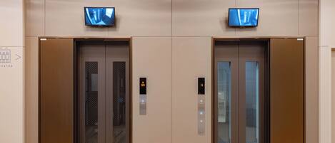 Two elevator doors with digital displays, a wall-mounted sign, and a tiled floor.