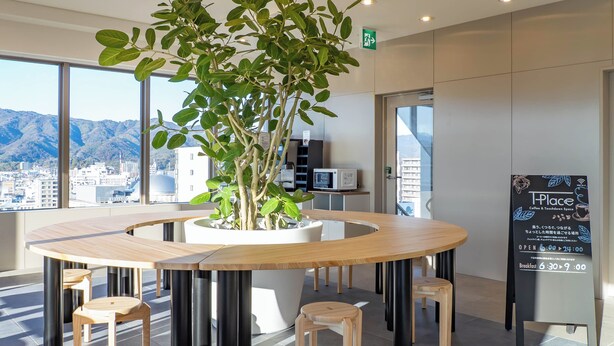 A modern interior with a round table surrounded by stools, a potted plant, and a signboard. - Toyoko Inn Kochi (Kochi)