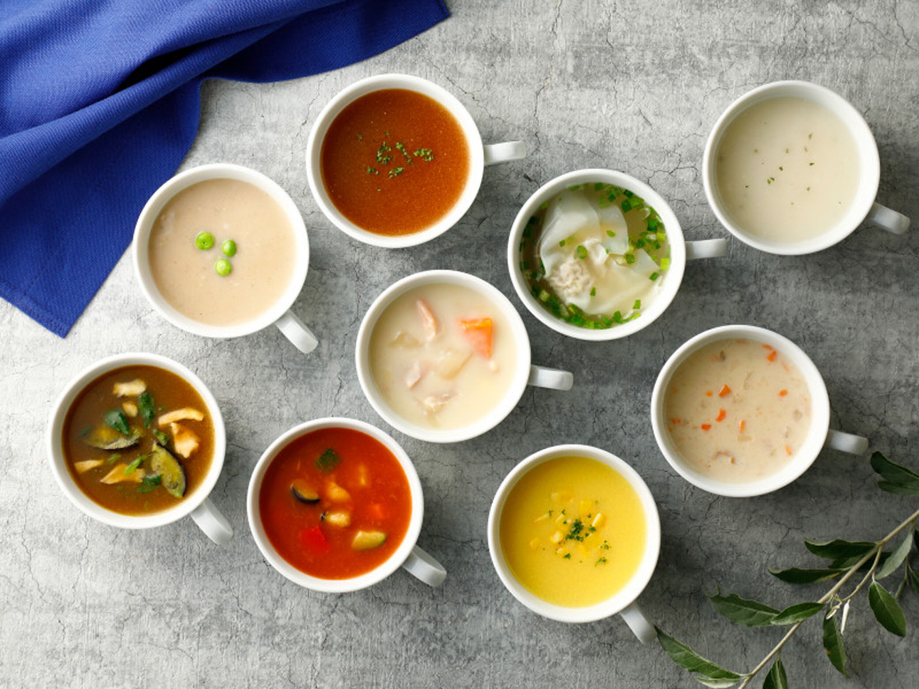 Nueve tazones de sopa dispuestas sobre una mesa con un mantel azul.