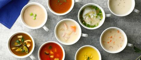 Nine bowls of soup arranged on a table with a blue cloth.
