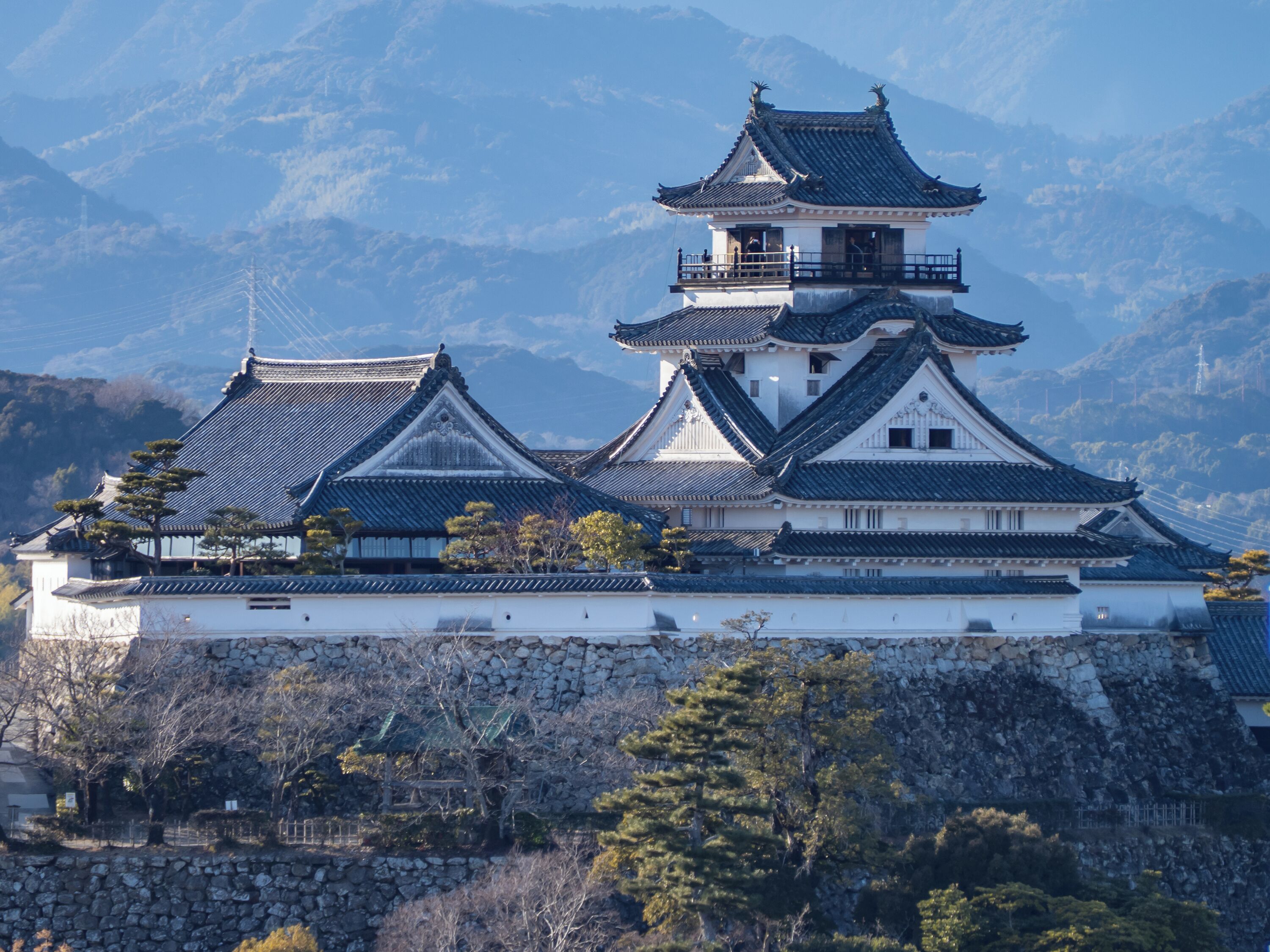 A traditional Japanese castle with multiple tiers, stone walls, and a mountainous backdrop.