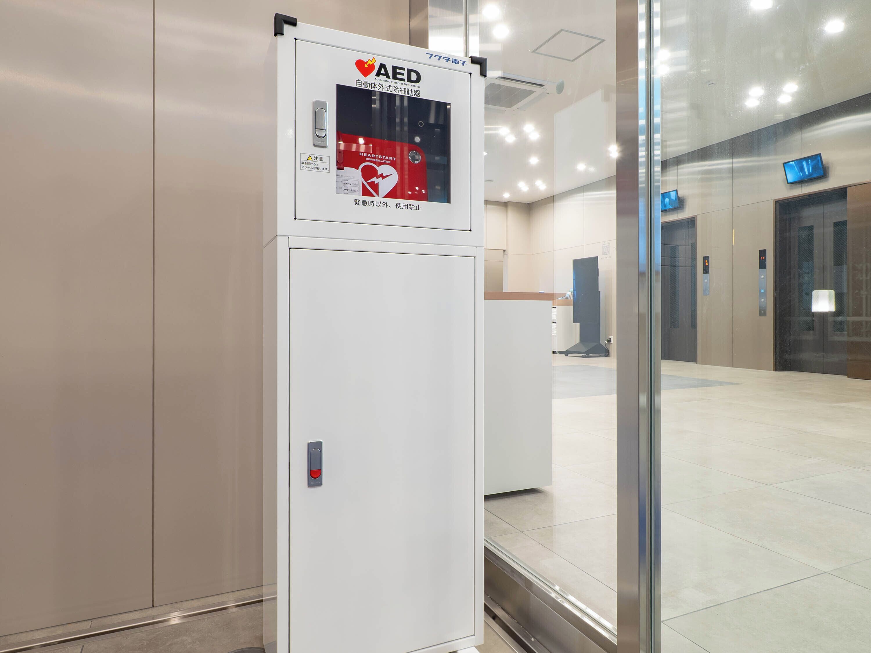 Un equipo de respuesta de emergencia para desfibrilación automática (DEA) blanco en un edificio moderno con puertas de cristal y suelo de baldosas.