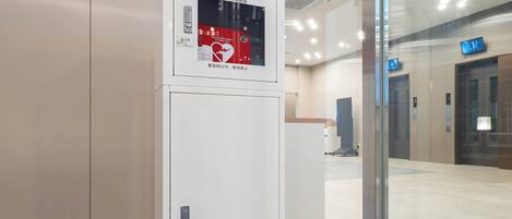Un equipo de respuesta de emergencia para desfibrilación automática (DEA) blanco en un edificio moderno con puertas de cristal y suelo de baldosas.