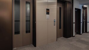 A hallway with elevator doors, a digital display, and a carpeted floor. - Toyoko Inn Kochi (Kochi)