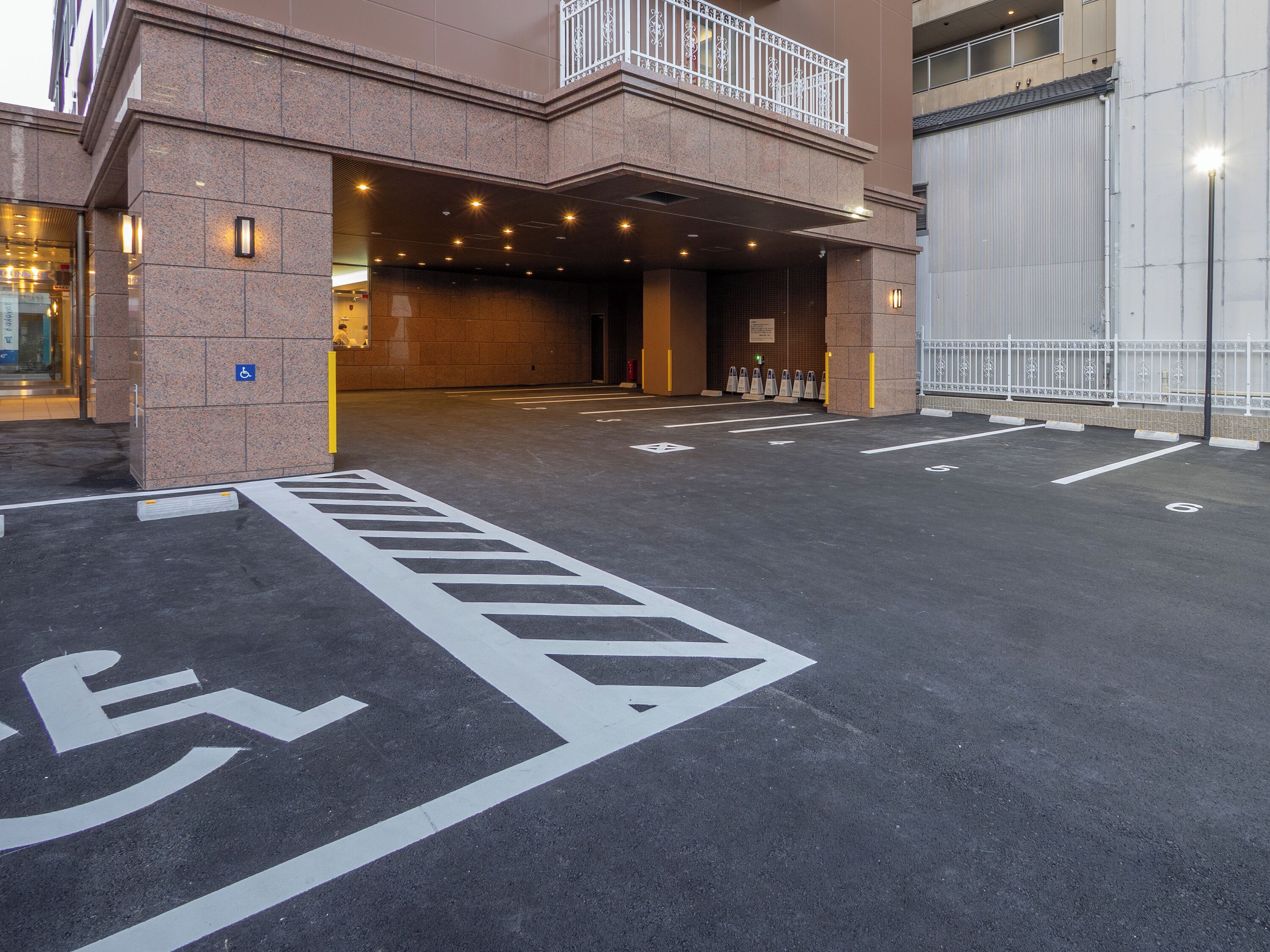 Un área de estacionamiento con señalización de accesibilidad para personas con discapacidad, entrada a un edificio y salida con barreras.