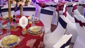 Ein Festsaal mit runden Tischen, weißen Stühlen und floralen Tischdekorationen.