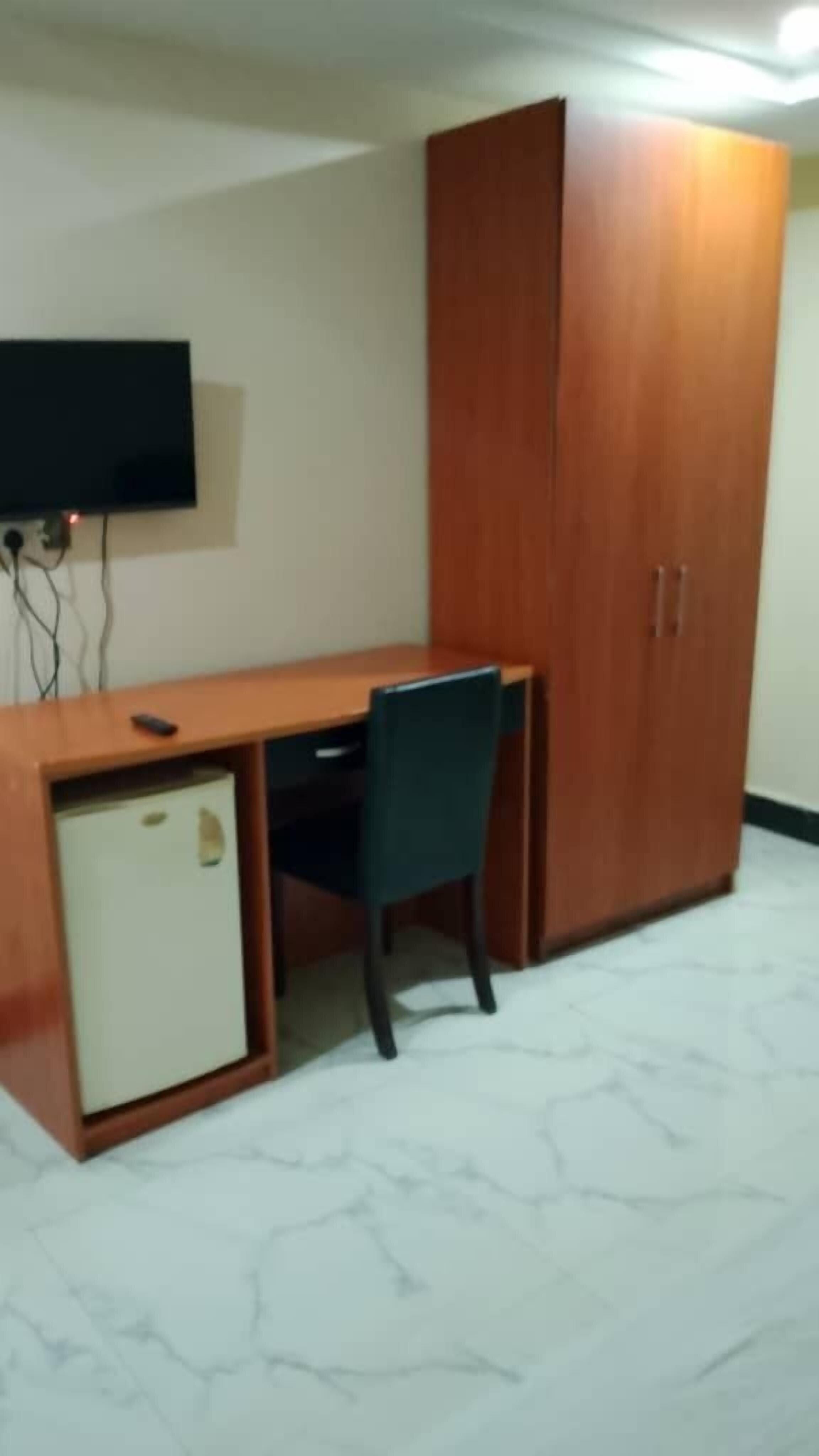 Une pièce comprenant un bureau en bois, une chaise, un téléviseur fixé au mur et une armoire.