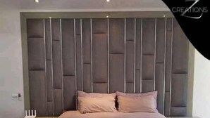 Ein modernes Schlafzimmer mit einer gepolsterten Kopfteile, einem großen Bett mit einer beige farbenen Bettdecke und einem Nachttisch mit einer Lampe.