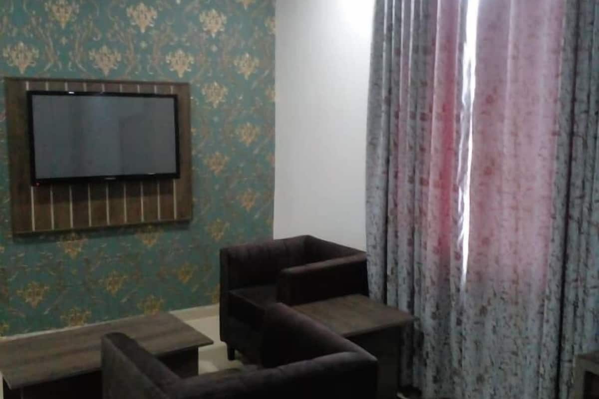 Ein Wohnzimmer mit gemustertem Wandpapier, einem an der Wand montierten Flachbildfernseher und einer Sofagarnitur.