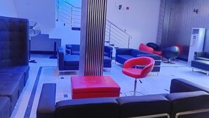 Ein moderner Lounge-Bereich mit schwarzen und roten Sitzmöbeln, einer zentralen Säule und einer Treppe im Hintergrund.
